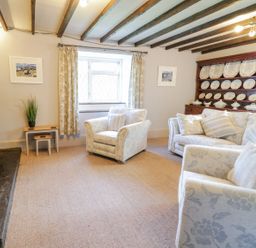 A living room with armchairs and a sofa near a window and a wooden cupboard with decorative plates at Dwynant in Bontddu near Dolgellau