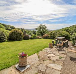 A backyard garden with a stone patio table bench chairs and flower pots at Dwynant in Bontddu near Dolgellau