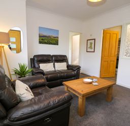 A living room with two leather sofas a wooden coffee table a floor lamp and wall art at Gilfach Bach in Dolgellau