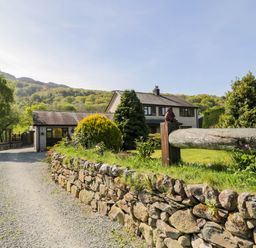 A gravel driveway leading to a house with a stone wall and trees at Gilfach Bach in Dolgellau