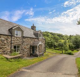 A stone cottage next to a curved paved driveway with trees and greenery in the surrounding area at Ty Glan Yr Afon in Bontddu near Dolgellau
