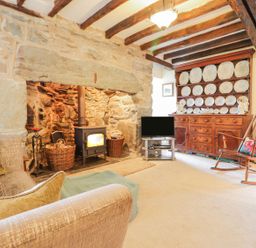 A living room with a stone fireplace wood stove wooden cupboard with plates rocking chair and sofa at Ty Glan Yr Afon in Bontddu near Dolgellau