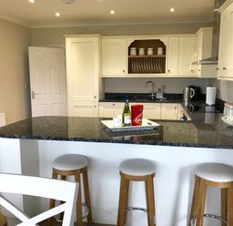 A kitchen with three wooden stools at a black countertop and cream cabinets at Pen Y Frith Bungalow in Prestatyn