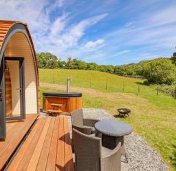 A wooden pod with outdoor seating and a hot tub in a grassy field at Briallen in Bontddu near Dolgellau