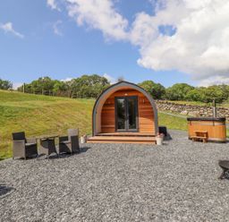 An outdoor area with a wooden pod cabin a hot tub a table with chairs and a fire pit at Eirlys in Bontddu near Dolgellau