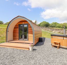 A wooden pod with double glass doors and a small wooden hot tub on gravel outside at Eirlys in Bontddu near Dolgellau
