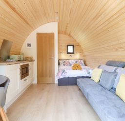 An arched wooden interior with a bed at the end and a kitchen area on the left and a sofa on the right at Eirlys in Bontddu near Dolgellau
