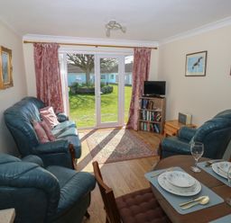 A living room with blue leather sofas a small TV on a bookshelf and a dining table set with plates and glasses at Kites - 52 Gower Holiday Village Scurlage near Port Eynon and Rhossili