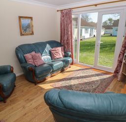A living room with blue leather sofas pink cushions a rug and a TV near large sliding glass doors at Kites - 52 Gower Holiday Village Scurlage near Port Eynon and Rhossili