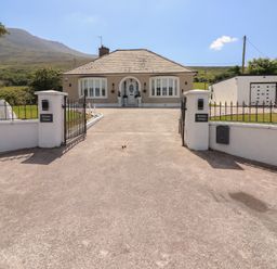 A bungalow house with a driveway and gated entrance set against a mountain backdrop at Killelton Cottage in Camp County Kerry