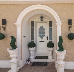 Front door entrance with white door under an archway flanked by potted topiary plants and hanging round greenery at Killelton Cottage Camp County Kerry