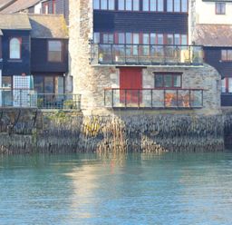 Stone and wood waterfront buildings with balconies over a stone seawall and water at Tobys Quay in Falmouth