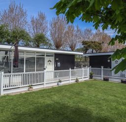 A grassy yard with potted plants and white railing outside single-story buildings at 99 Cherry Park in Chapel St Leonards