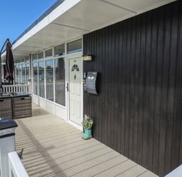 A porch with a white door black wall and outdoor furniture at 99 Cherry Park in Chapel St Leonards