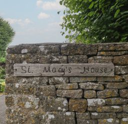 A stone wall with a wooden sign displaying the name St. Mary's House at St. Marys House Church Westcote near Bledington