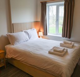 A bedroom with a bed, nightstand, and window at Bedroom 7 in Penrith