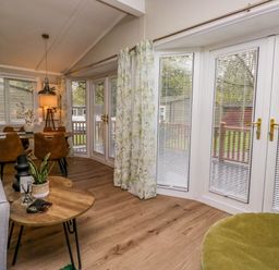 A living room with a wooden table and chairs a gray sofa and a green chair with floral curtains at Robins Lodge White Cross Bay near Troutbeck Bridge