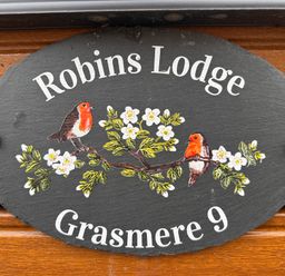 An oval black sign with two birds on a flowered branch and text robins lodge grasmere 9