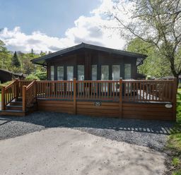 A wooden lodge with a front deck and steps surrounded by trees and grass at Robins Lodge White Cross Bay near Troutbeck Bridge
