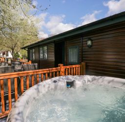 An outdoor deck with a hot tub and wicker chairs next to a wooden cabin at Robins Lodge in White Cross Bay near Troutbeck Bridge