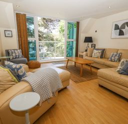 A living room with beige sofas a wooden coffee table and a glass door leading to a balcony at 6 Red Sails in Sandbanks