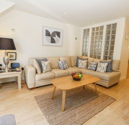 A living room with a beige sectional sofa and patterned cushions a wooden coffee table with a bowl of fruit a table lamp and vintage telephone on a side table at 6 Red Sails in Sandbanks