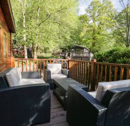 An outdoor balcony with wicker furniture including a table and chairs surrounded by trees at Mere Brook Lodge in White Cross Bay