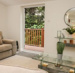 A living room with brown sofa a glass table plants and an open door to a wooden deck at Mere Brook Lodge in White Cross Bay