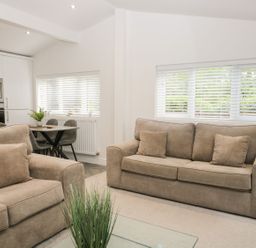 A living room with two beige sofas and a small dining table with chairs near a kitchen at Mere Brook Lodge in White Cross Bay