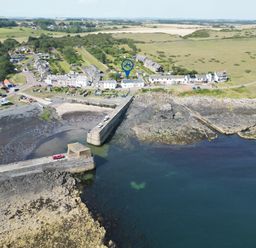 An aerial view of a village near the coast with a pier and parked vehicles at Puffin Cottage in Craster