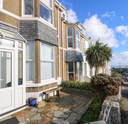 A row of houses along a street with parked cars and a stone patio with a bench at Breakers Point in St Ives