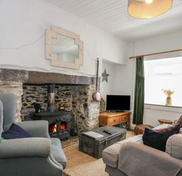 A living room with a wood stove fireplace armchairs a sofa a coffee table and a television at Cobweb Cottage in Waunfawr