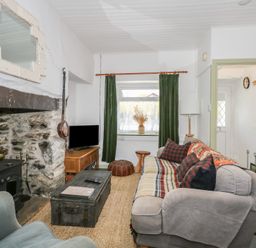 A living room with a stone fireplace a sofa armchair coffee table and television at Cobweb Cottage in Waunfawr