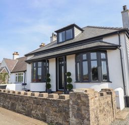 A detached house with a stone wall and a front door flanked by two topiary plants at Bronallt in Cemaes Bay