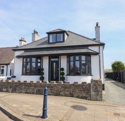 A detached house with black framed windows and door a stone wall and a driveway at Bronallt in Cemaes Bay