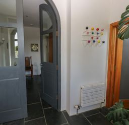 An entryway with dark arched double doors a colorful coat rack on the wall a small radiator and a large leafy plant at Zoar Chapel in Carew