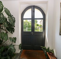 An entrance with a dark arched double door a large leafy plant a mirror on the wall and a small wooden bench at Zoar Chapel in Carew