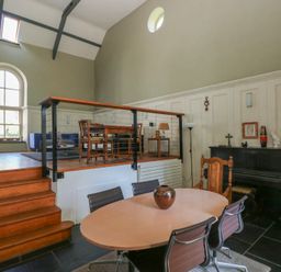 A split-level room with a dining table and chairs on the lower level and a sitting area with chairs and a table on the upper level at Zoar Chapel in Carew