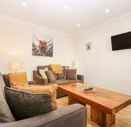 A living room with brown sofas a wooden coffee table a wall-mounted television and artwork at Smiddy Bothy in Edzell