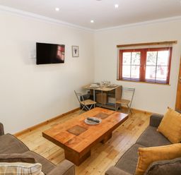 A living room with two sofas a wooden coffee table a wall-mounted TV and a small dining table with two chairs at Smiddy Bothy Edzell