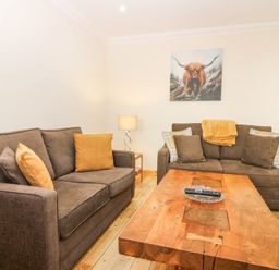 A living room with two brown sofas a wooden coffee table a lamp and a painting of a bull at Smiddy Bothy in Edzell