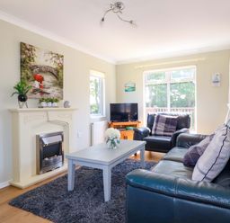 A living room with a fireplace a gray coffee table black leather sofas and a TV at Lodge 9- Lamorna Tregolds near St Merryn