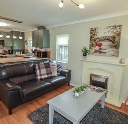 A living room with a sofa, coffee table, and kitchen area at Lodge 9 - Lamorna Tregolds near St Merryn