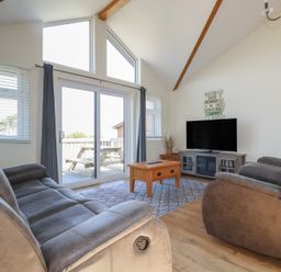 A living room with brown sofas a wooden coffee table a television and sliding glass doors leading to an outdoor picnic table at Lodge 18 in St Merryn