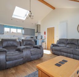 A living room with grey sofas a wooden coffee table and a kitchen with blue cabinets at Lodge 18 in St Merryn