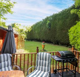 A garden with chairs, table, grill, and a patio umbrella at Stumps Cross Lodge, Upper Coscombe near Winchcombe