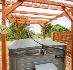 An outdoor hot tub under a wooden pergola with string lights at Woodpecker in Lode near Bottisham