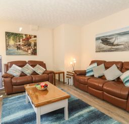 A living room with two brown leather sofas a wooden coffee table with a fruit bowl a blue rug and paintings on white walls at Old Malthouse Apartment in Weymouth