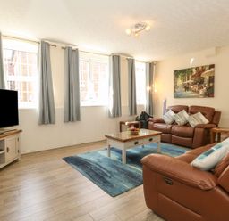 A living room with brown leather sofas a coffee table and a television at Old Malthouse Apartment in Weymouth