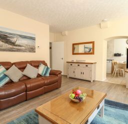 A living room with a brown leather sofa and cushions a wooden coffee table with a bowl of fruit and a television on a stand at Old Malthouse Apartment in Weymouth